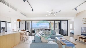 Ein modernes Wohnzimmer mit einer Couch, einem Couchtisch und einem Fernseher. Ein Balkon bietet Blick auf Gebäude.