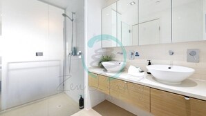 Ein modernes Badezimmer mit Duschkabine aus Glas, einem weißen Waschbecken und Holzschränken.