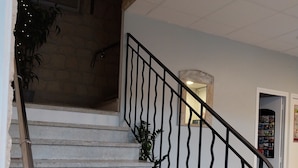 Eine Treppe mit Metallgeländer, ein Blumentopf und ein Stuhl in einem Raum mit Fliesenboden und einer Tür, an der ein Bulletin Board angebracht ist.