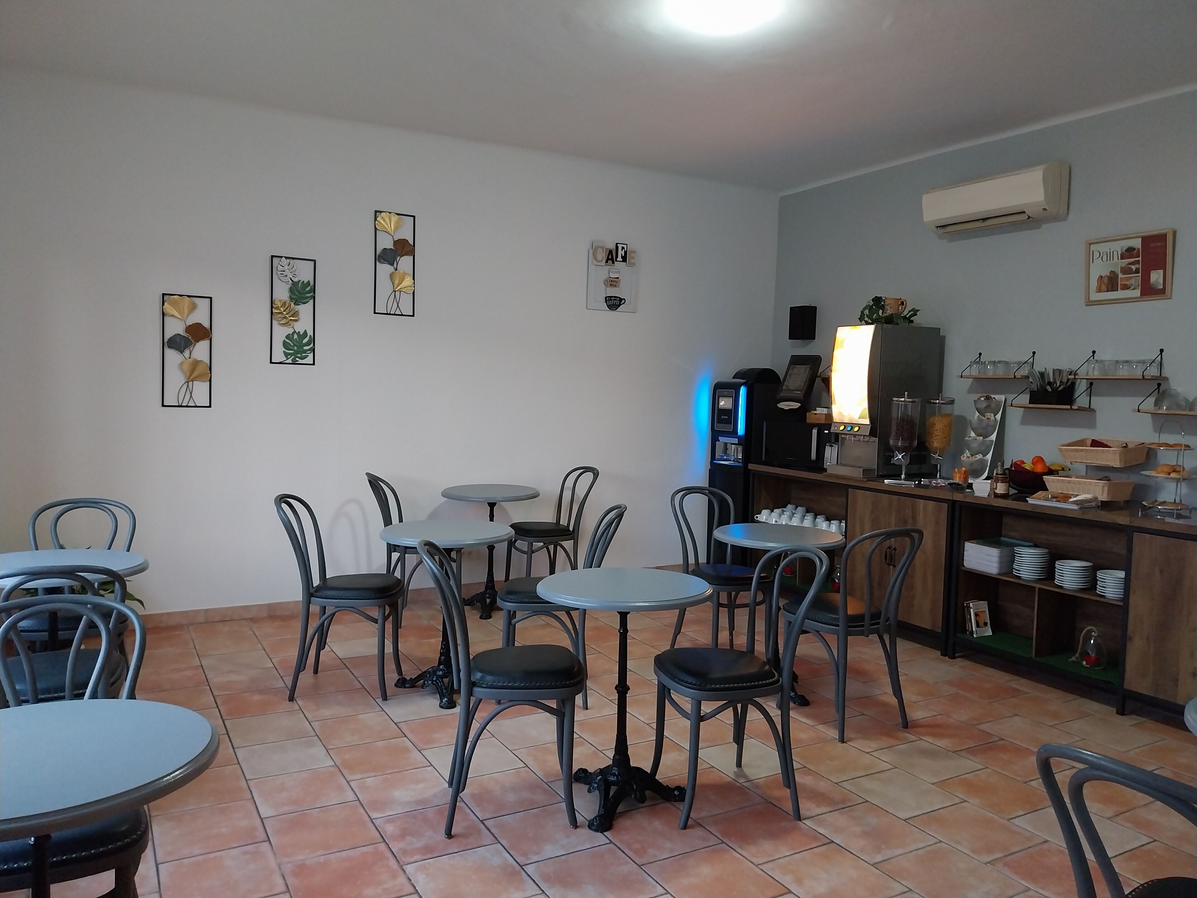 Una cafetería con varias mesas y sillas, una máquina de café y una zona de bufé con diversas opciones de comida.