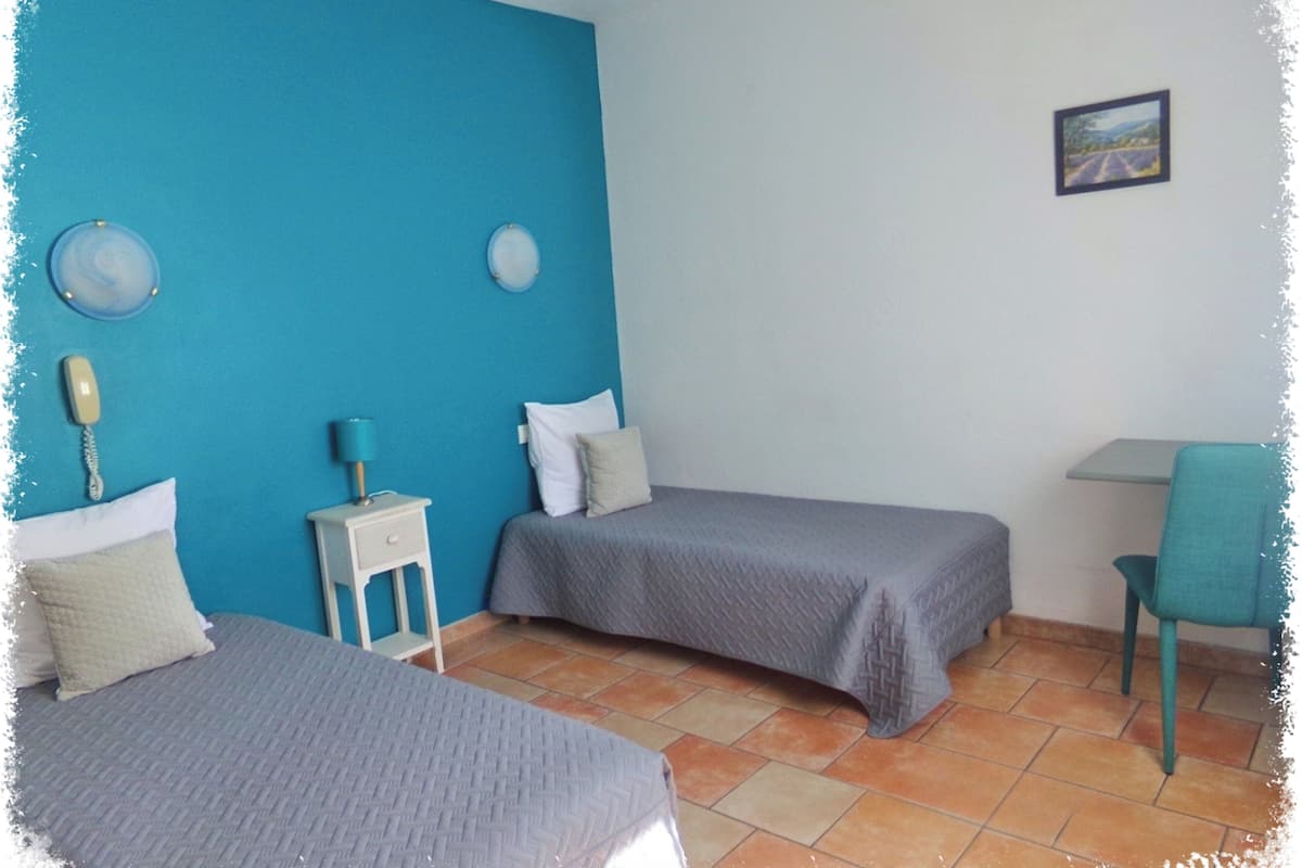 Une chambre avec deux lits, une petite table, une chaise et un tableau accroché au mur.