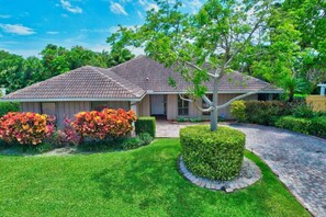 A two-story house with a tiled roof, surrounded by well-maintained lawns and flowering bushes. - Idyllic Boca Pool Home: 4/2.5 + Study-FAU & Mizner (Boca Raton)