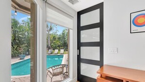 A room with a sliding glass door leading to a pool area, a wooden desk, and a framed target on the wall. - Idyllic Boca Pool Home: 4/2.5 + Study-FAU & Mizner (Boca Raton)