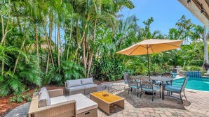 An outdoor patio with wicker furniture, a pool, and lush tropical vegetation. - Idyllic Boca Pool Home: 4/2.5 + Study-FAU & Mizner (Boca Raton)