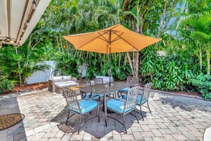 An outdoor patio with a table and chairs, surrounded by lush greenery. - Idyllic Boca Pool Home: 4/2.5 + Study-FAU & Mizner (Boca Raton)