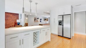 A modern kitchen with white cabinetry, a wooden accent wall, pendant lighting, and a stainless steel refrigerator. - Idyllic Boca Pool Home: 4/2.5 + Study-FAU & Mizner (Boca Raton)