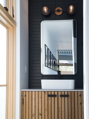 A bathroom with a white sink, a large mirror, and wooden cabinetry. - The Lunawood - Lux Home Pool and Spa (Joshua Tree)