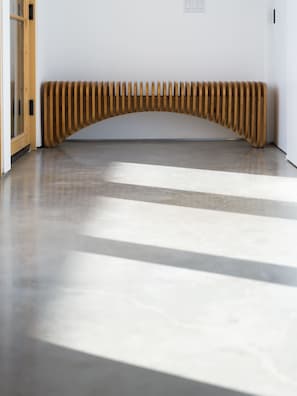 A modern interior with a wooden bench against a white wall, a polished concrete floor, and a door with a glass panel.