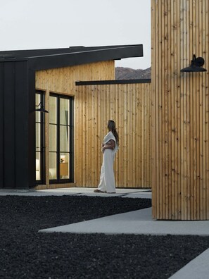 A modern building with a wooden exterior, a glass door entrance, and a concrete ground. - The Lunawood - Lux Home Pool and Spa (Joshua Tree)