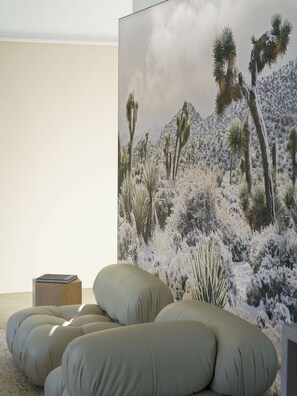 A room with a large painting of a desert landscape, a sofa, and a small table with a book. - The Lunawood - Lux Home Pool and Spa (Joshua Tree)