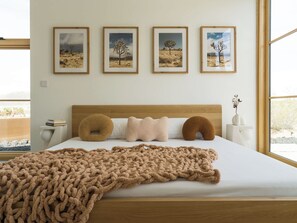 A bedroom with a bed, pillows, a blanket, and four framed pictures on the wall.