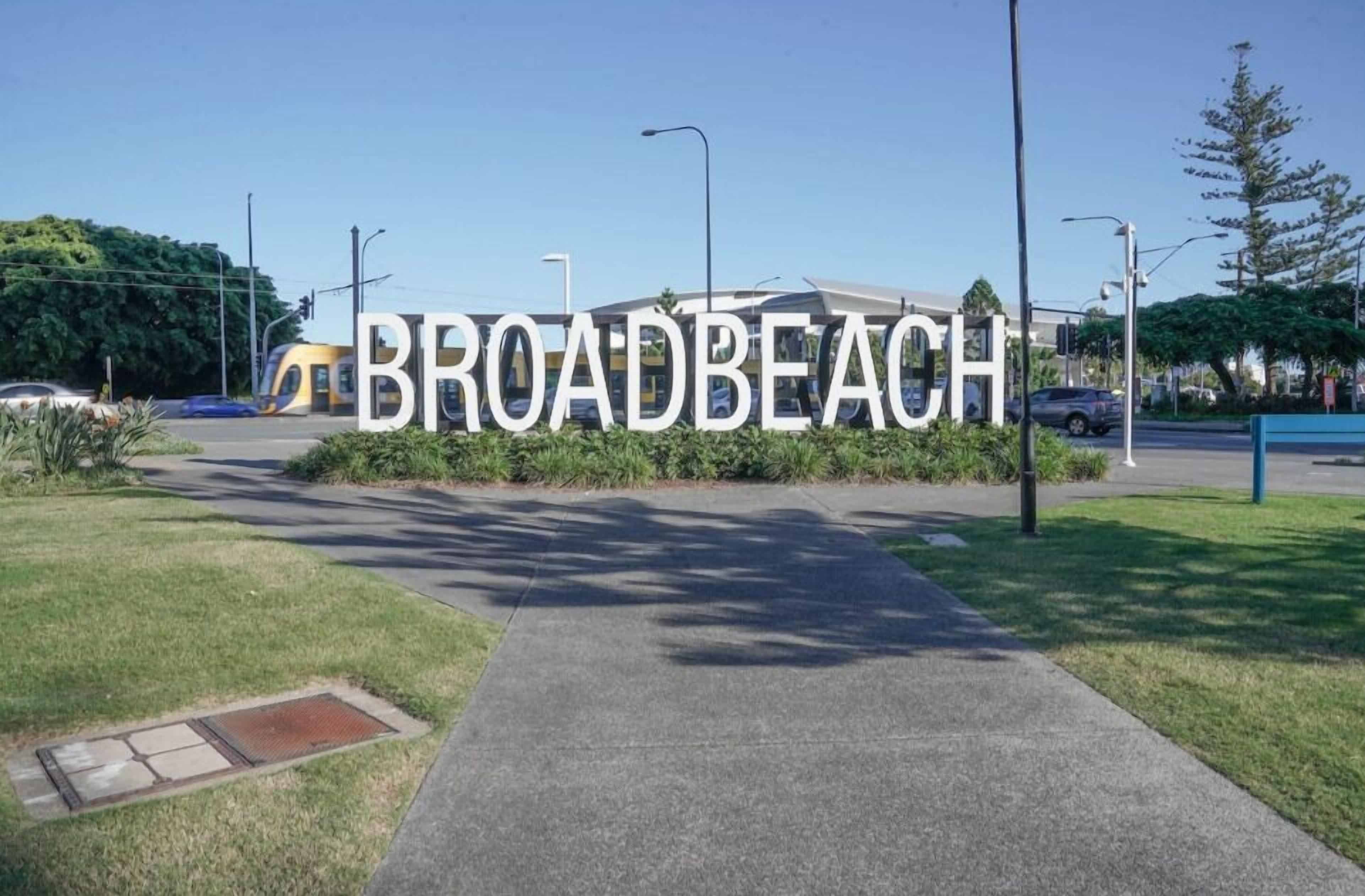 Een bord met de tekst 'BROADBEACH' en een duidelijk pad dat naar een gebouw leidt.