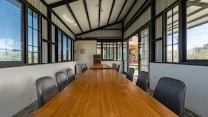 Un salón de conferencias con una larga mesa de madera, varias sillas y ventanas amplias.