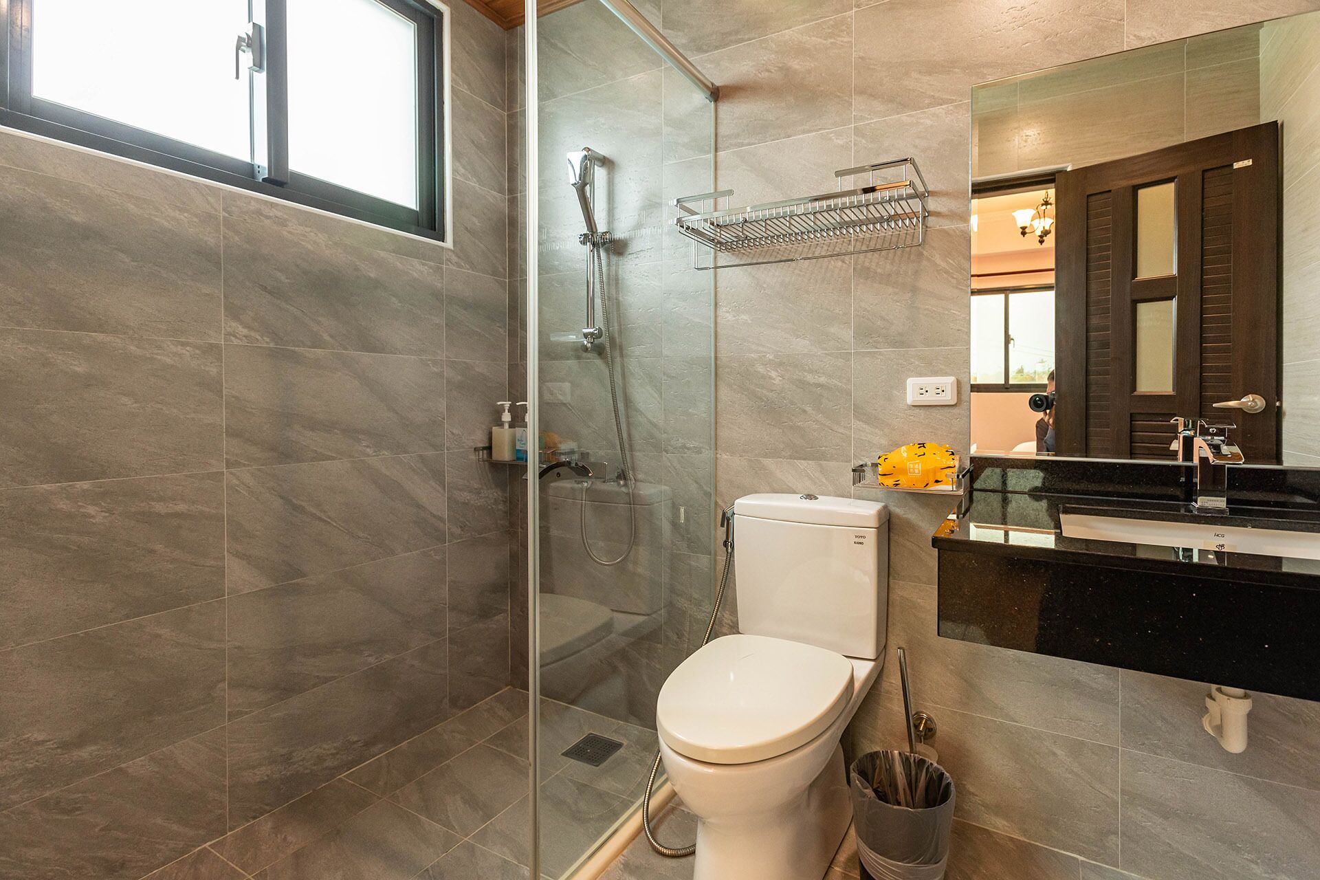 A modern bathroom with a glass-enclosed shower, a toilet, and a sink with a mirror above.