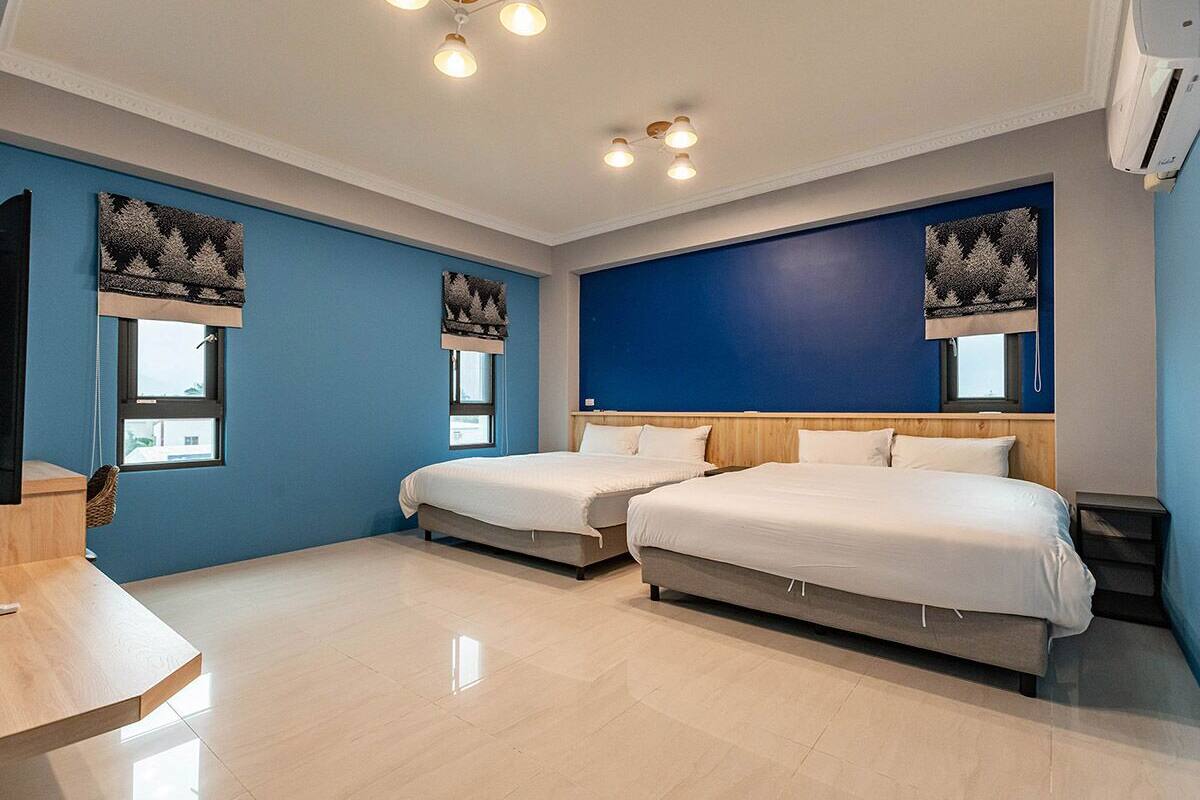 A modern hotel room with two beds, a wooden desk, and a large window.