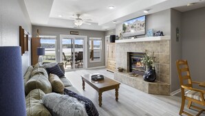 A spacious living room with a fireplace, a television, and a view of the outdoors. - Ozark Overlook – Waterfront, Two Pools, Tennis, and More! (Lake Ozark)