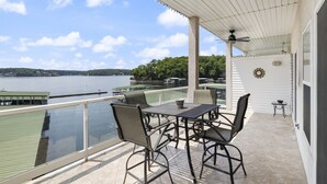 A covered outdoor seating area with a table and chairs, overlooking a body of water and a dock. - Ozark Overlook – Waterfront, Two Pools, Tennis, and More! (Lake Ozark)