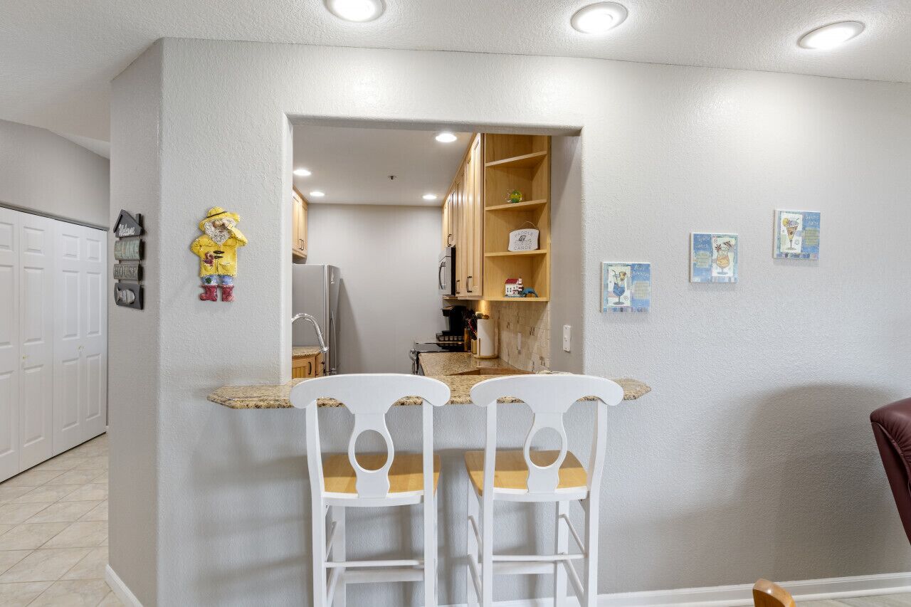 Een compacte keuken met een centraal kookeiland, witte barstoelen en een koelkast.