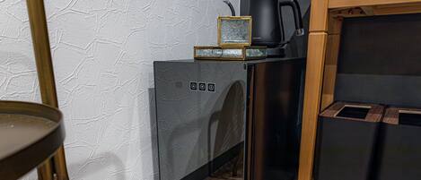 A compact kitchen with a modern design, featuring a black refrigerator, a coffee maker, and a kettle on the countertop.