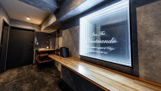 A modern interior with a reception desk, a large illuminated sign, and a dark-toned wall with a geometric pattern. - INN THE OMOTESANDO (Tokyo)