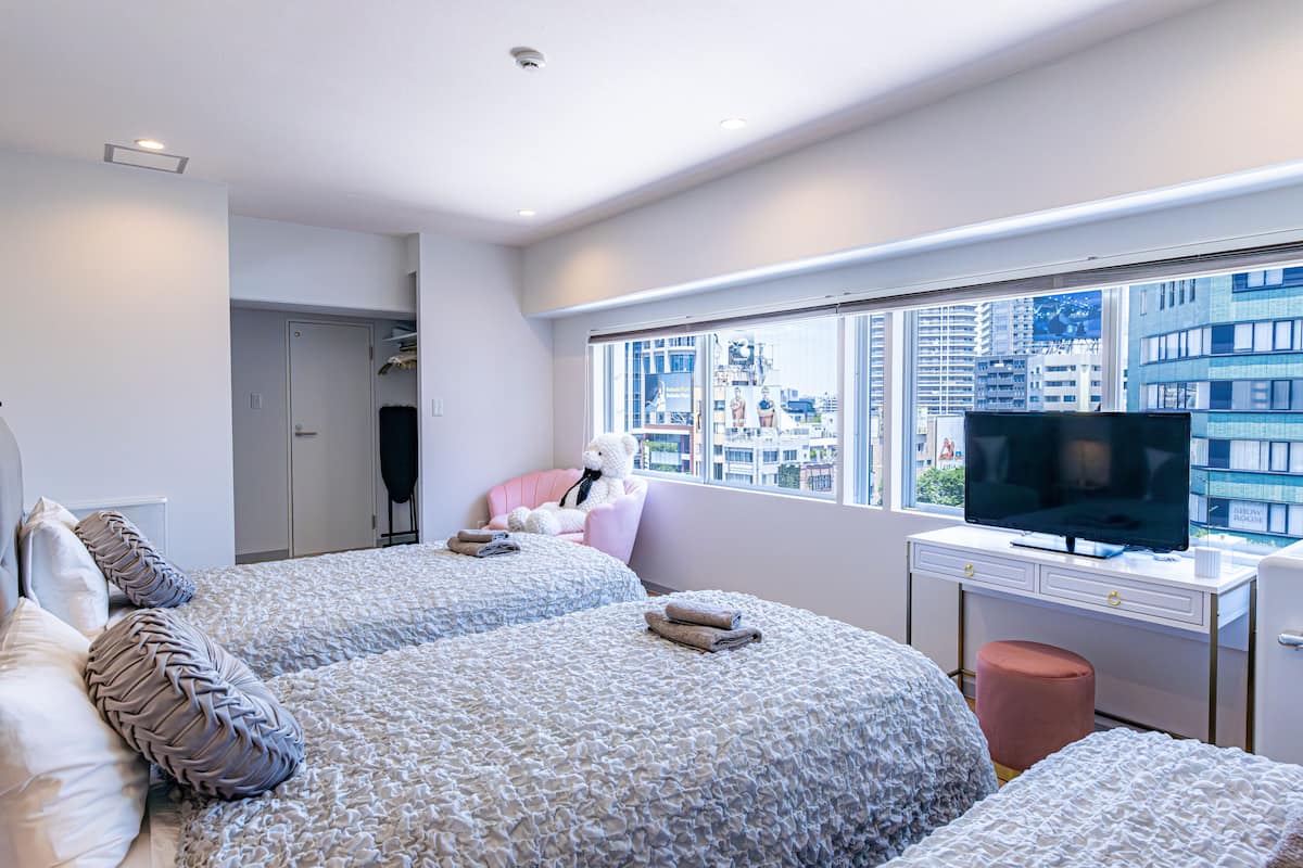 A modern hotel room with two beds, a television, and a large window offering a city view.