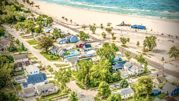 Vue aérienne d’une zone résidentielle côtière, avec des maisons, une plage et une vue dégagée sur l’océan.