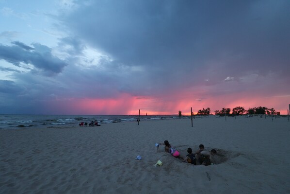 En strandscene med folk, der leger i sandet, og en solnedgang i baggrunden.