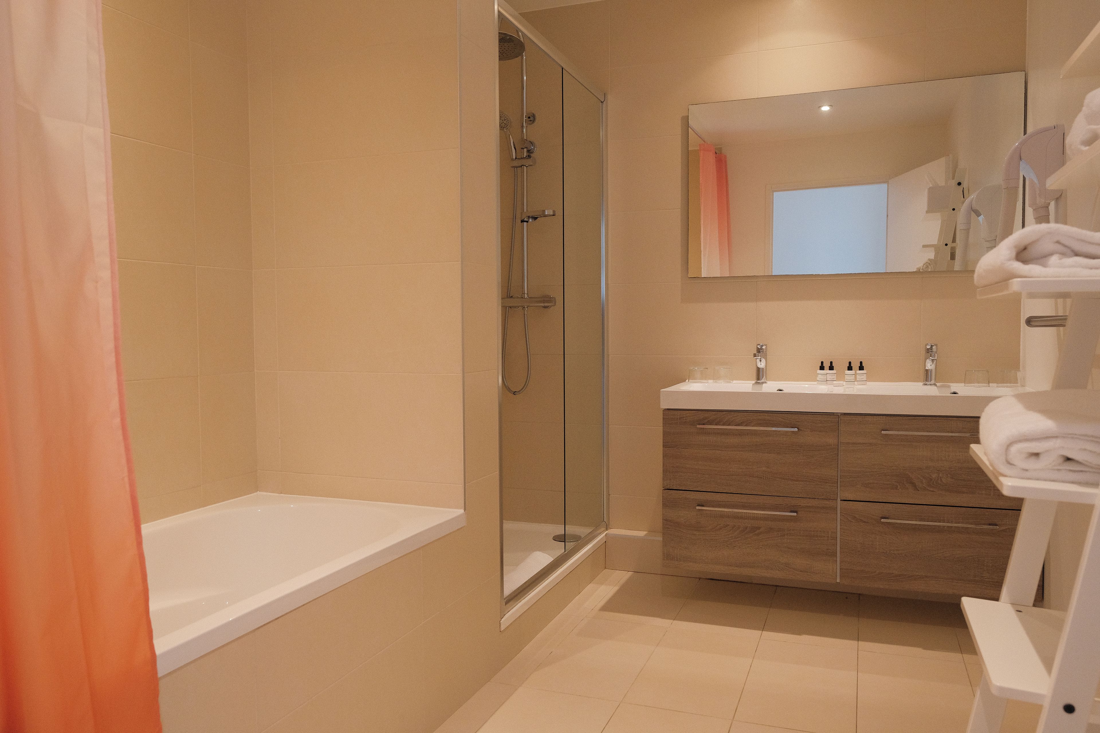 A modern bathroom with a glass-enclosed shower, a white bathtub, and a vanity with a mirror.