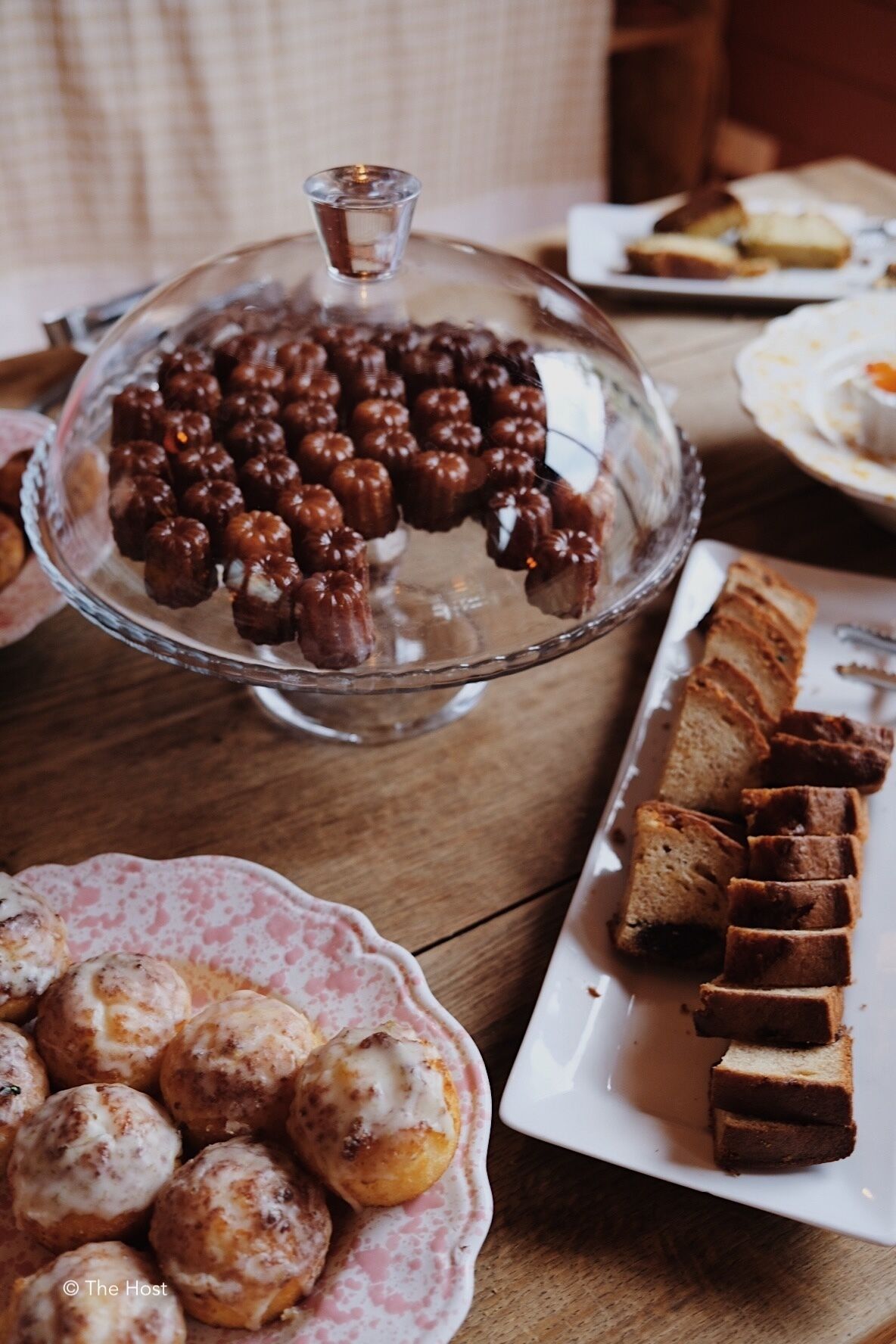 A table with various food items including a glass-covered chocolate dessert, bread slices, and round pastries.