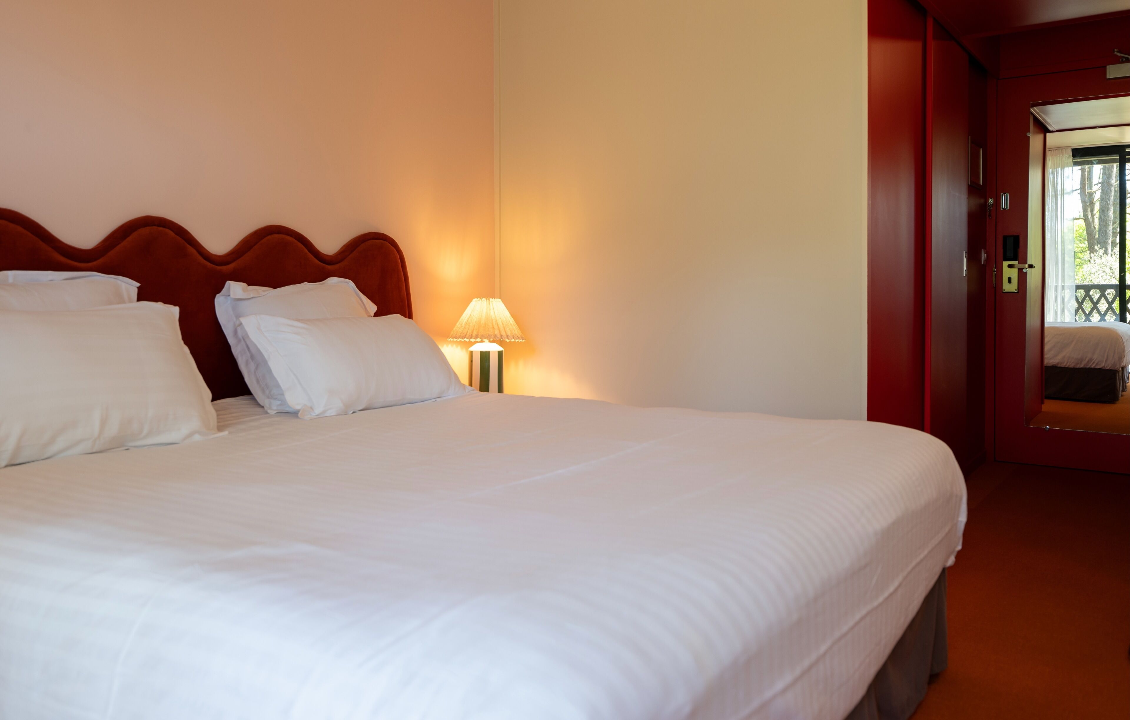 Ein Hotelzimmer mit einem großen Bett, einem Nachttisch mit Lampe und einer Tür, die auf einen Balkon führt.