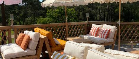 A wooden deck with outdoor seating, including sofas and chairs, under a large striped umbrella.