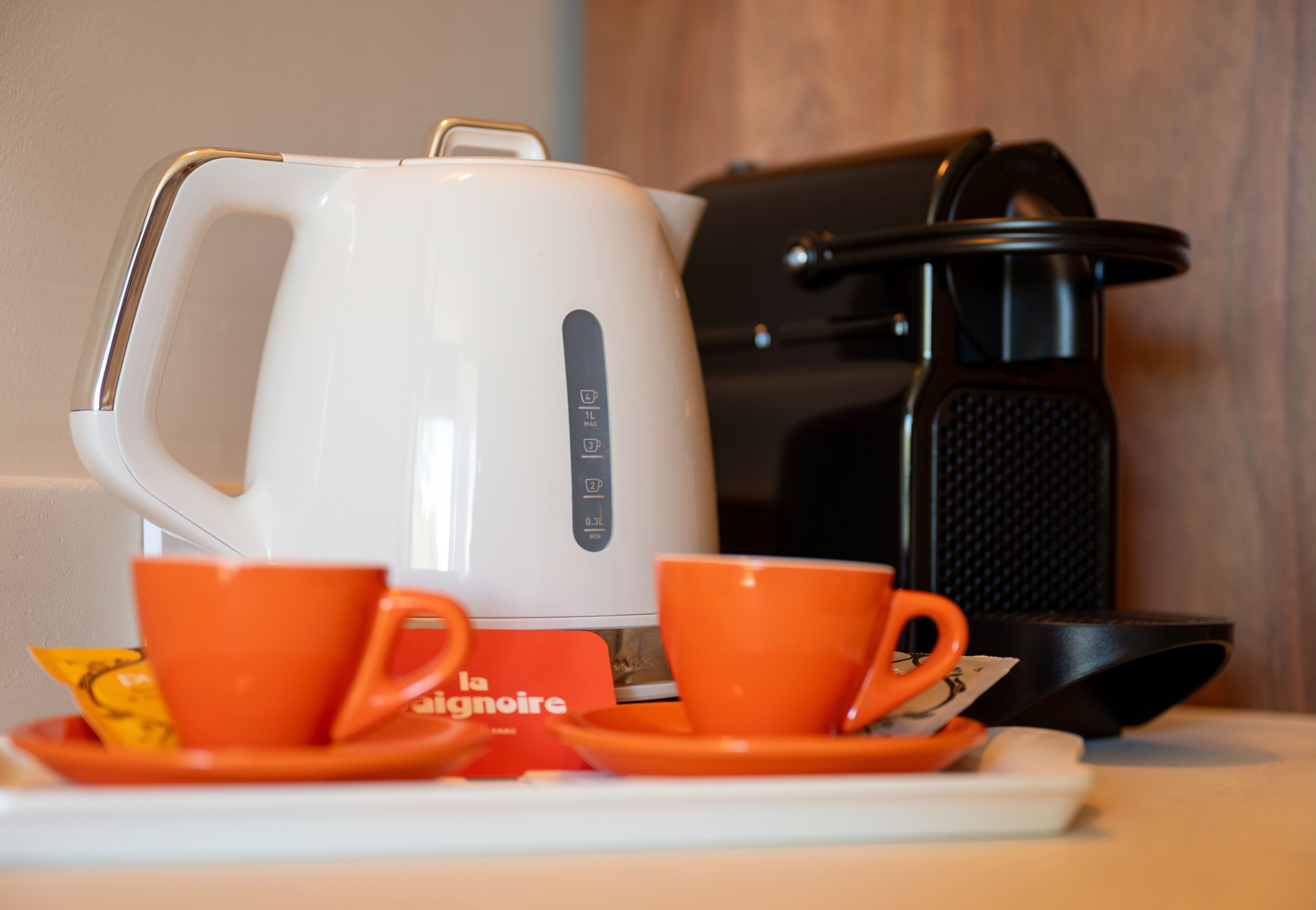 Une machine à café, deux tasses oranges et une soucoupe sur une table.