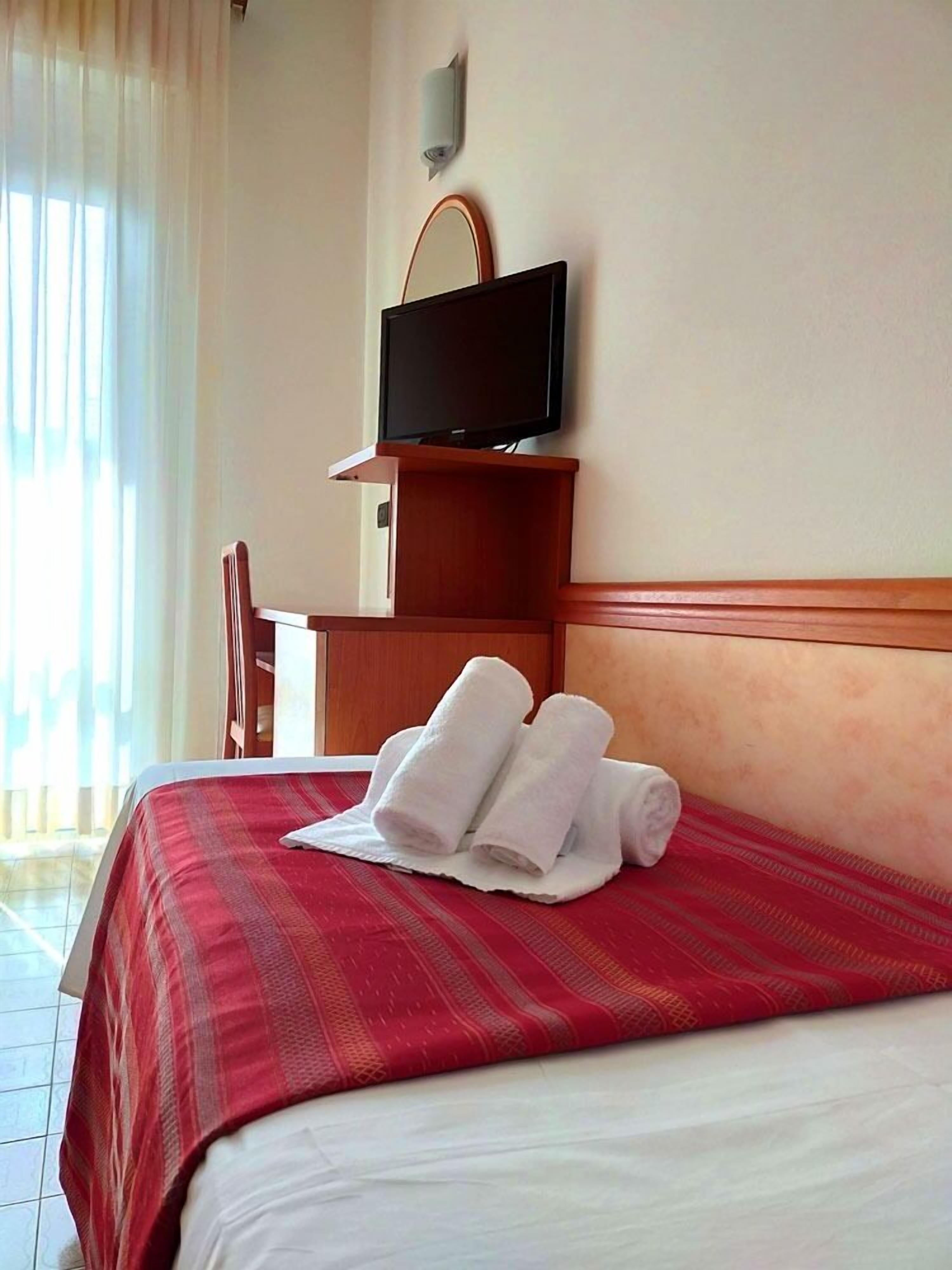 A hotel room with a bed, a television on a stand, and a desk with a chair.