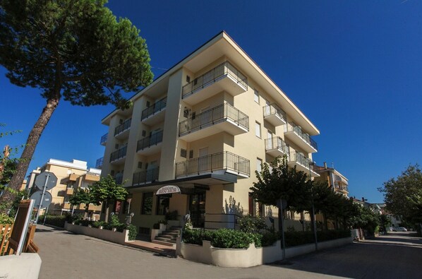 Un hôtel à plusieurs étages doté de balcons, d’une entrée principale et entouré de verdure.