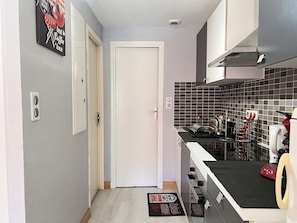Um corredor estreito leva a uma cozinha com painel de azulejos, decoração temática de café e um eletrodoméstico vermelho na bancada.