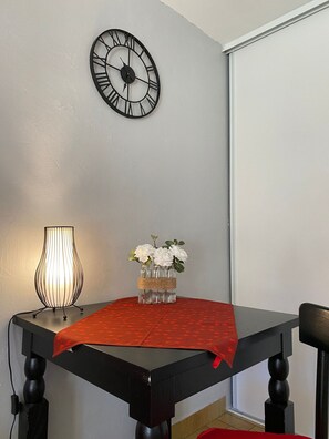 A dining table with a red tablecloth, a wall clock, and a vase with flowers. - T2 ensoleillé avec terrasse et vaste jardin commun (Cauterets)