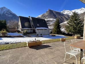 A chalet with a sloped roof, a wooden deck, and a view of snow-capped mountains.