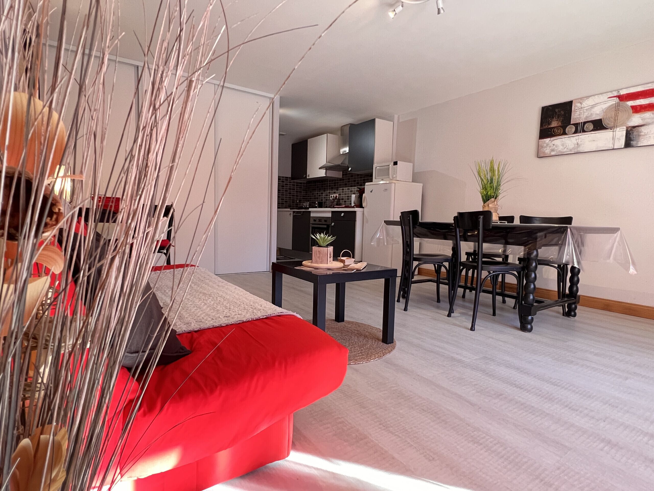 Una sala de estar moderna con un sofá rojo, un comedor con mesa y sillas, y una cocina al fondo.
