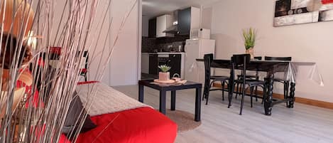 Una sala de estar moderna con un sofá rojo, un comedor con mesa y sillas, y una cocina al fondo.
