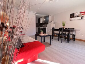 A modern living room with a red sofa, a dining area with a table and chairs, and a kitchen in the background.