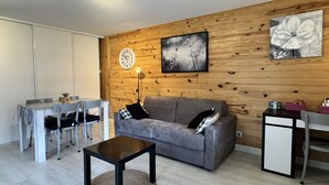 Ein modernes Wohnzimmer mit grauem Sofa, einer Holz-Akzentwand, einem runden Couchtisch und einem Essbereich mit weißem Tisch und Stühlen.