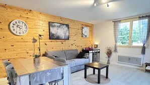 Ein modernes Wohnzimmer mit einer Holzverkleidung, einer runden Uhr, einem Sofa, einem Esstisch und einem Fenster mit Vorhängen.