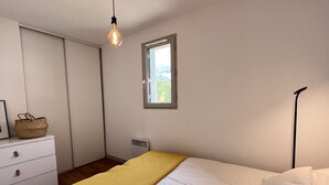 Un dormitorio con cama, ventana, radiador, cómoda y lámpara colgante.