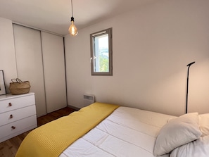 Ein Schlafzimmer mit Bett, Fenster, Heizkörper, Kommode und einer Pendelleuchte.