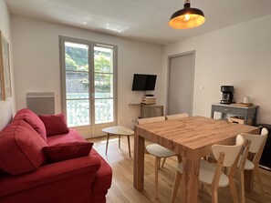 A compact living space with a sofa, dining table, chairs, a TV, and a coffee maker. - T3 centre ville avec parking, balcon et wifi. 5P. (Cauterets)