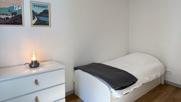 A bedroom with a single bed, a nightstand with a lamp, and two wall-mounted posters. - T3 centre ville avec parking, balcon et wifi. 5P. (Cauterets)