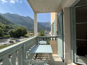 A balcony with a table and chairs, overlooking a mountain landscape and a road with parked cars. - T3 centre ville avec parking, balcon et wifi. 5P. (Cauterets)