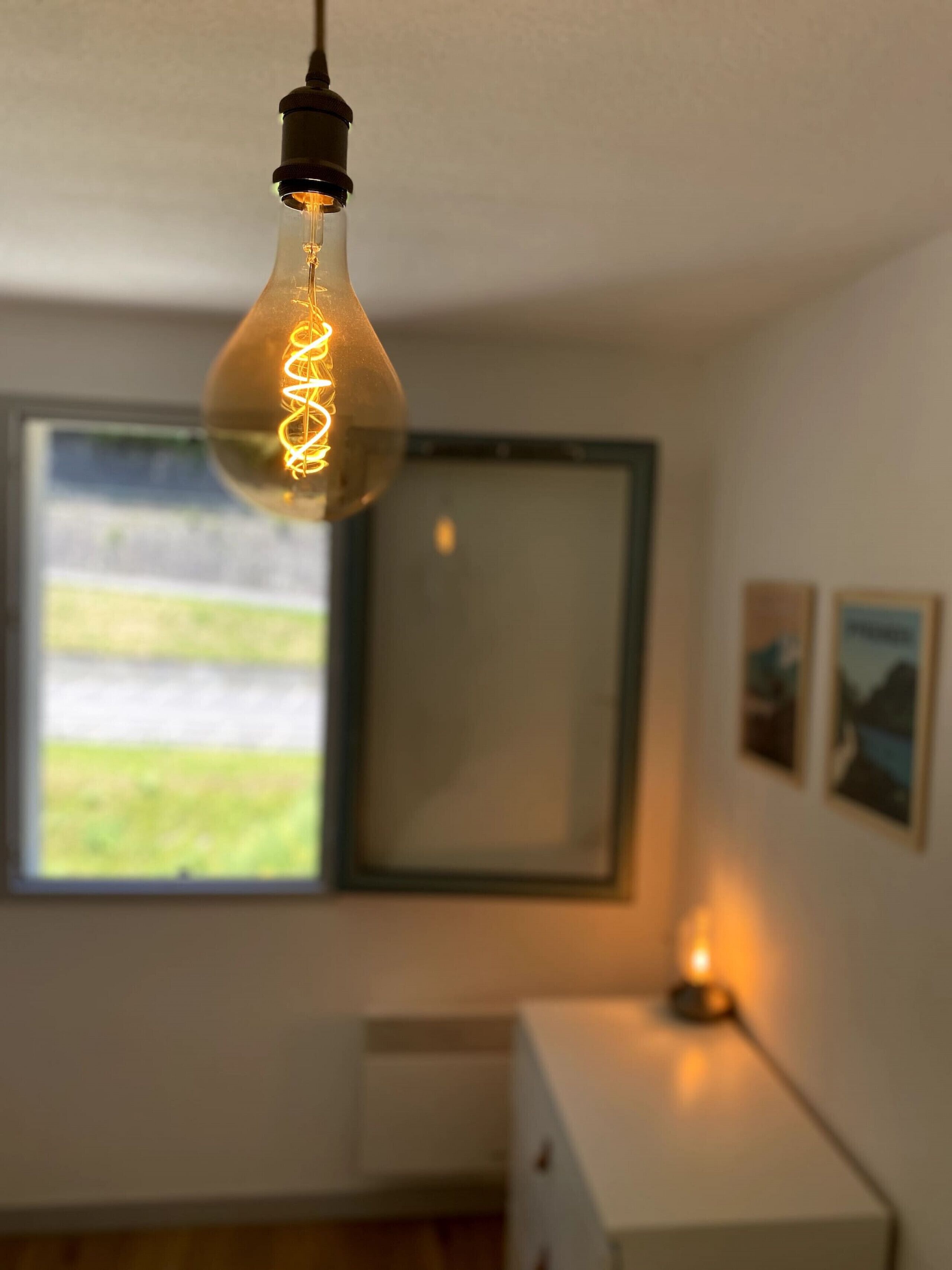 Una habitación con una lámpara colgante, una ventana con vistas y una mesita de noche con lámpara.