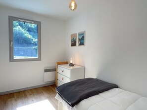 A bedroom with a bed, a nightstand, a window with a view of greenery, and a wall with two framed pictures. - T3 centre ville avec parking, balcon et wifi. 5P. (Cauterets)