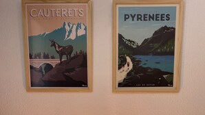 Dos carteles enmarcados con paisajes de 'Cauterets' y los 'Pirineos', y una mesa con una lámpara de vidrio iluminada.